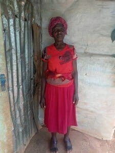A woman wearing a red skirt, top and headscarf stands in her home in Haiti. 